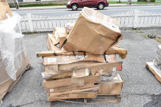 Damaged cardboard boxes stacked on a wooden pallet, with visible shipping labels indicating contents and origin.