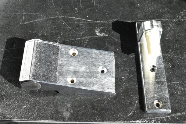 Metallic door hinge brackets, polished finish, with three visible screw holes each. Good condition.