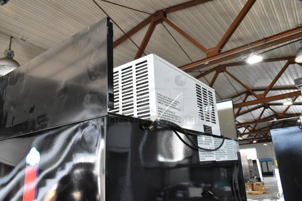Commercial refrigeration unit with black exterior, featuring a white top-mounted cooling system. Visible safety labels and power cables. Good condition.