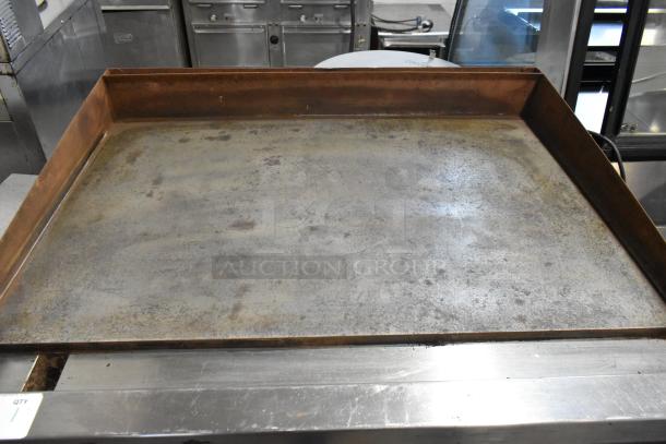 Rustic, large metal griddle in used condition, showing some surface wear. Suitable for commercial cooking use.