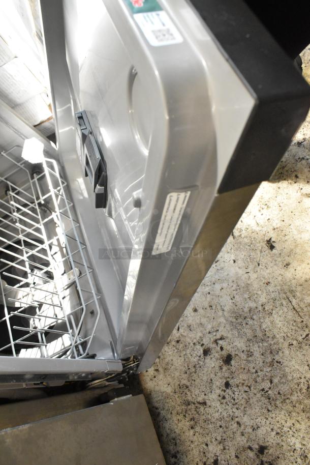Stainless steel dishwasher with open door, interior racks visible. Tags show model and serial numbers. Slight wear on exterior.