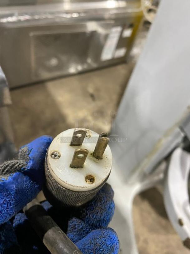 Three-prong electrical plug with wear marks, held by gloved hand.