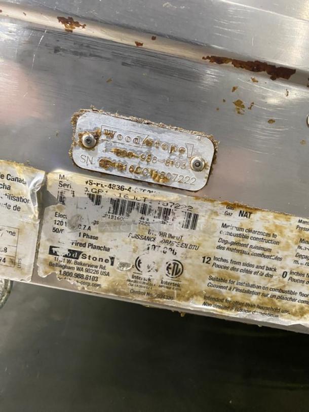 Metal kitchen equipment with visible wear, featuring a Wood Stone label and serial number. Labels show model VS-PL-4836-A-3700 and indicate electrical specs and usage instructions.