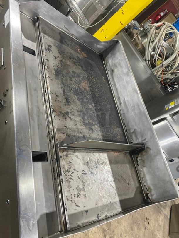 Commercial stainless steel flat top griddle, used condition with visible wear and discoloration, large cooking surface.