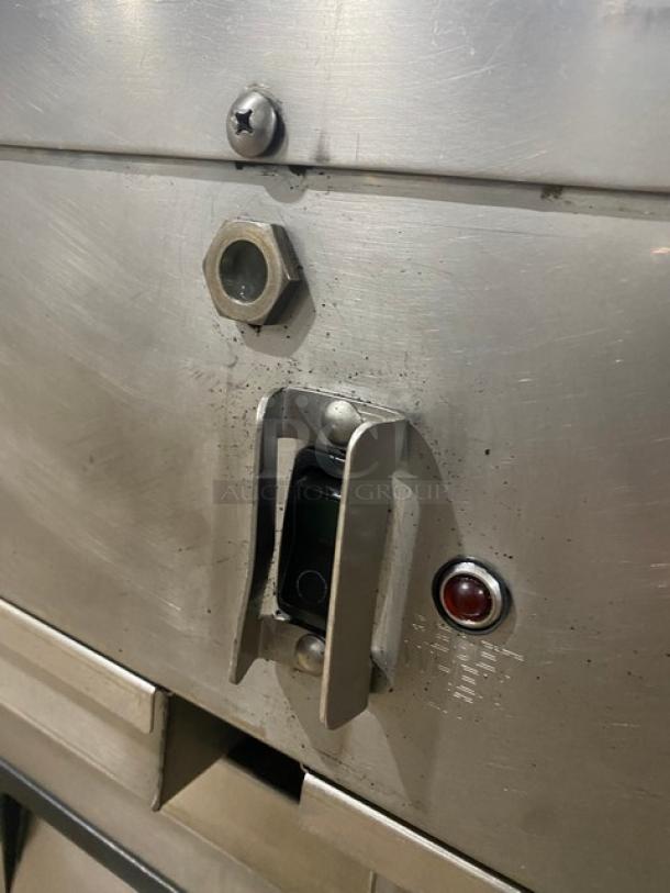Industrial stainless steel equipment panel with a toggle switch, red indicator light, and hex bolt. Slightly worn.