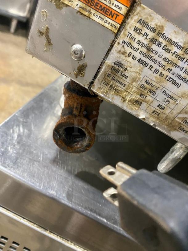 Rusty gas appliance fitting with plug on metal surface. Label indicates gas type and altitude information, showing signs of wear.