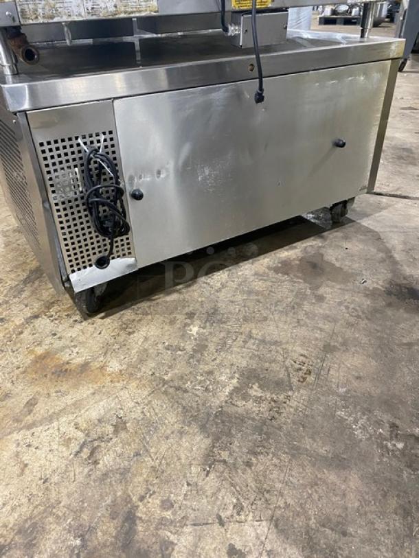 Stainless steel commercial refrigeration unit, rolling casters, vented side panel with wiring, visible dents, industrial use.