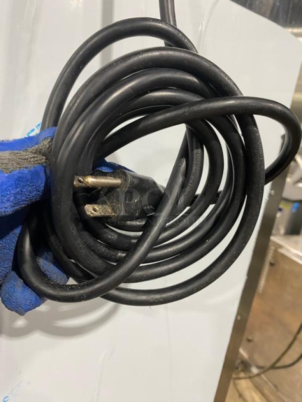 Black extension cord with a standard three-prong plug, in good condition. Coiled and held by a gloved hand.