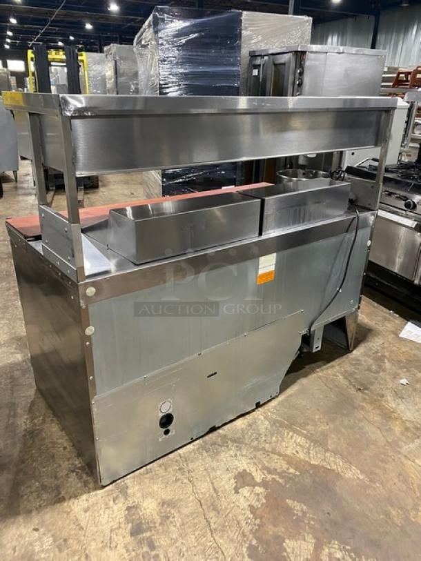 Commercial stainless steel food warmer with upper heated shelf, visible power cord, and condition tag on front.