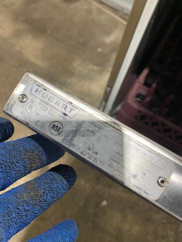 Hobart commercial dishwasher model tag, indicating serial number and NSF certification, held by a person in blue gloves.