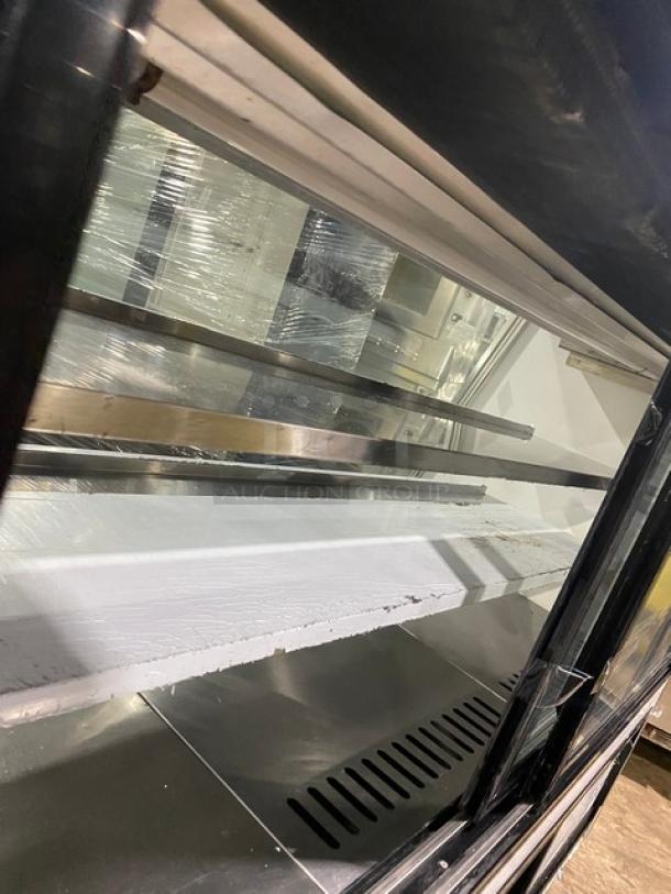 Large commercial display case with glass panels, metal shelving, and ventilation slots. Used condition, wrapped in plastic.
