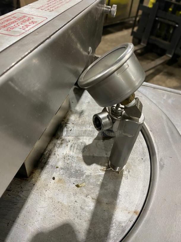 Stainless steel pressure gauge on a metal surface, industrial use, slight wear.