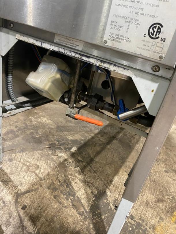 Commercial kitchen equipment, underside view with gas fittings and labeled panel indicating pressure settings and certifications.