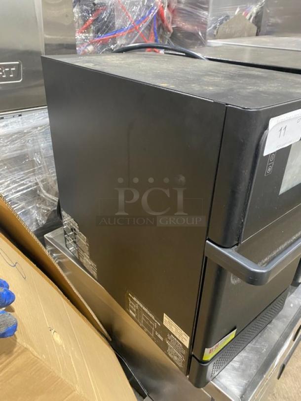 Black industrial microwave with side control panel, model labels visible. Used condition with some surface wear.