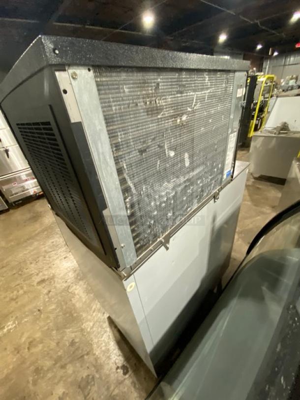 Commercial ice machine with visible wear, metal casing, ventilation panels, and control labels. Rugged, industrial condition.