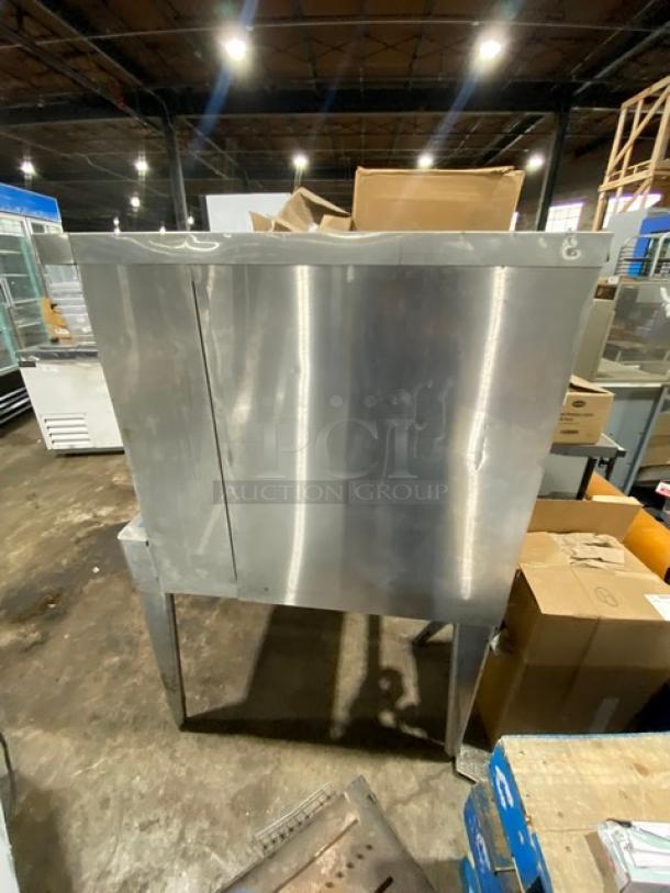 Stainless steel commercial ice bin on legs, dented surface, no visible brand, viewed in warehouse setting.