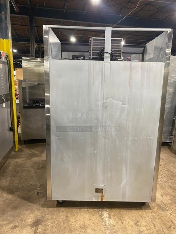 Commercial stainless steel refrigeration unit with visible scratches and dents; rear cooling coils; industrial setting.