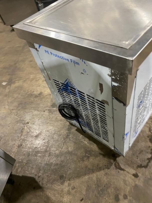 Commercial stainless steel refrigerator with visible PE protective film, minor wear, vent detailing, and coiled power cord.