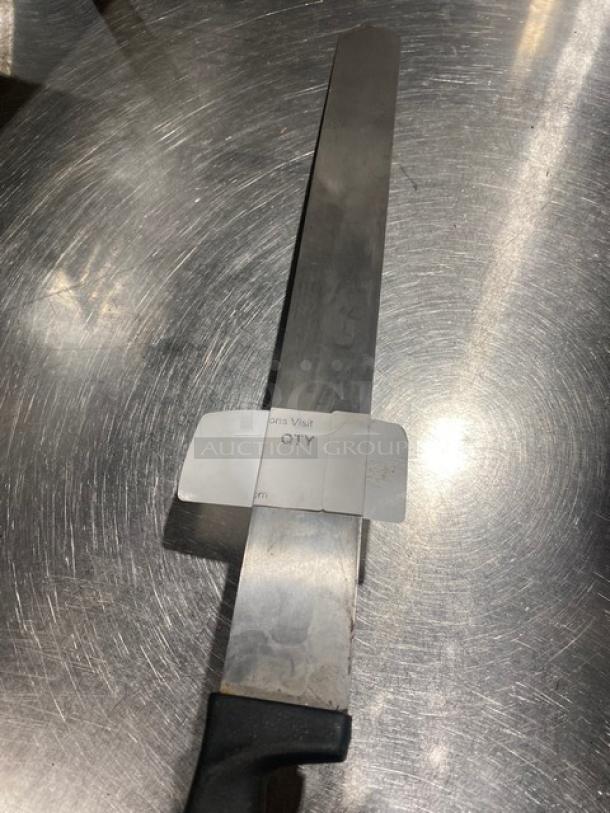 Large stainless steel knife with black handle on metal surface, marked with a label showing "ONS Visit QTY". Good condition.