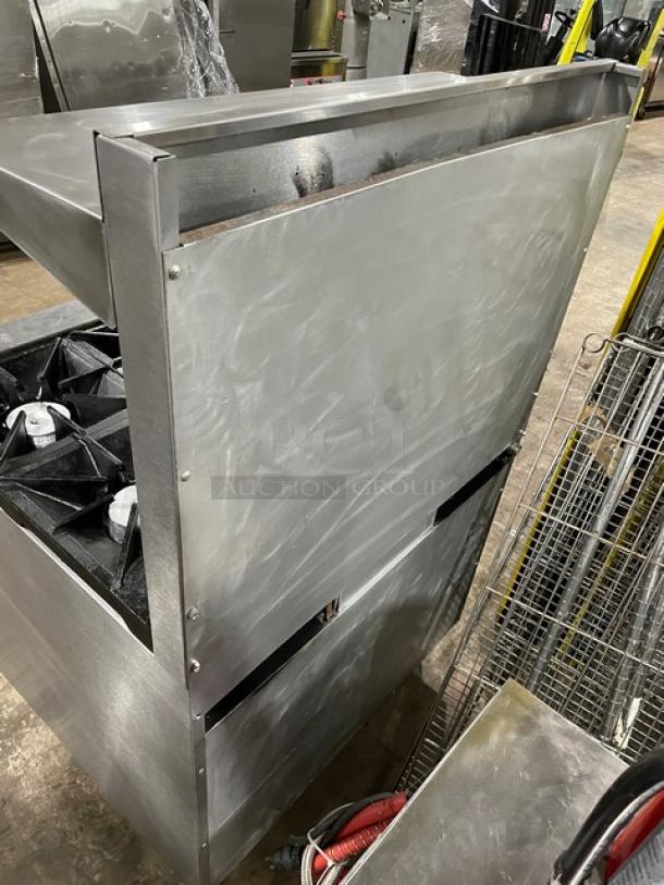 Stainless steel commercial gas stove with multiple burners, used condition, visible scuff marks, industrial setting.