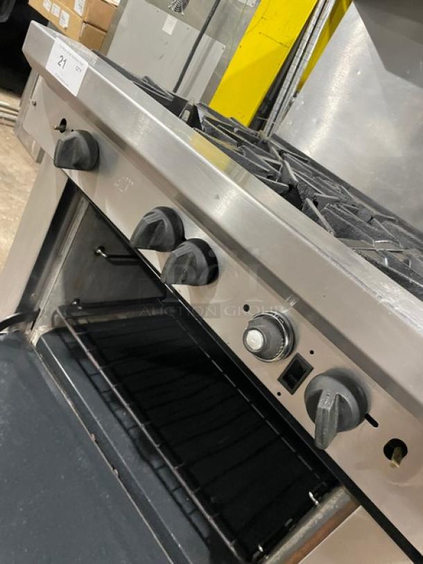 Stainless steel commercial gas stove with four burners, open oven door, control knobs intact, minimal wear, label "21".