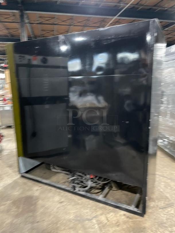 Black industrial control panel enclosure, large size, matte finish, visible wiring, located in a warehouse.