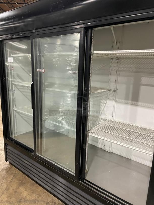 Commercial glass door refrigerator, three sliding doors, metal shelving, black exterior, used condition, spacious interior.
