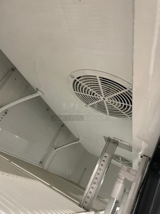 Commercial refrigerator interior, white finish, metal shelving, ceiling vent fan, sturdy construction, clean, well-maintained condition.