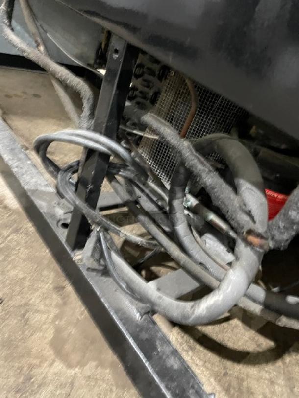 Industrial equipment with metal frame and coiled hoses, showing visible wear. Rear panel and grid structure partially visible.