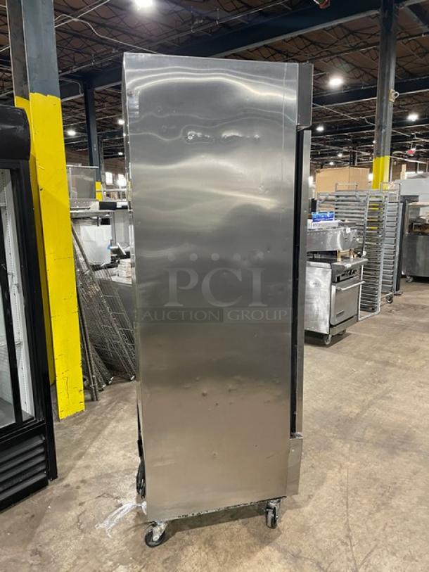 Stainless steel commercial refrigerator on casters, used condition with some dents, suitable for restaurant or catering use.