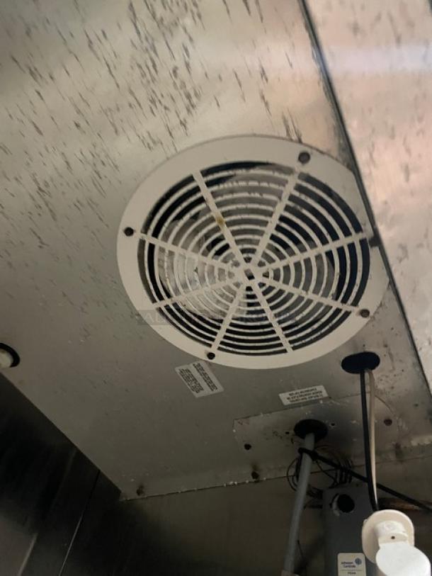 Industrial metal vent fan with protective grille, visible wiring, and condition markings, suitable for commercial use.