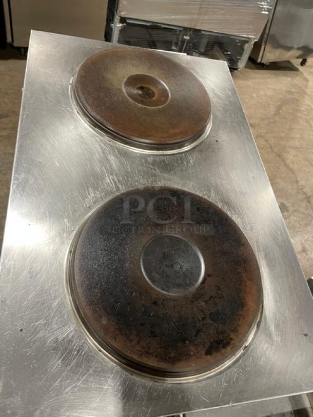 Commercial stainless steel stove top with two large iron burners, showing signs of heavy use and wear.