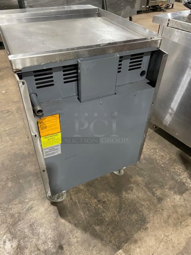 Commercial metal griddle on wheels with ventilation slots, side handle, safety labels, and visible wear. Ideal for industrial kitchens.