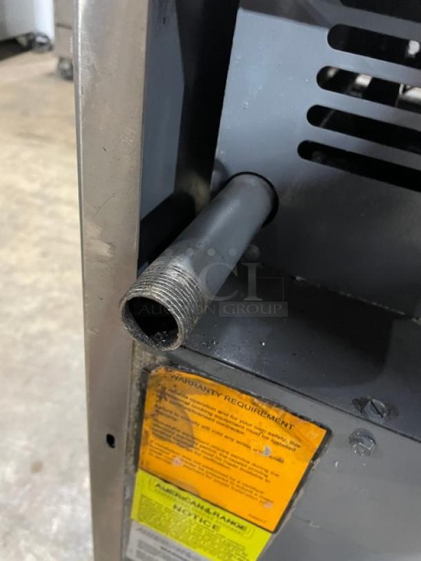 Metal machinery with a threaded pipe, visible warning label detailing warranty requirements, in used condition.