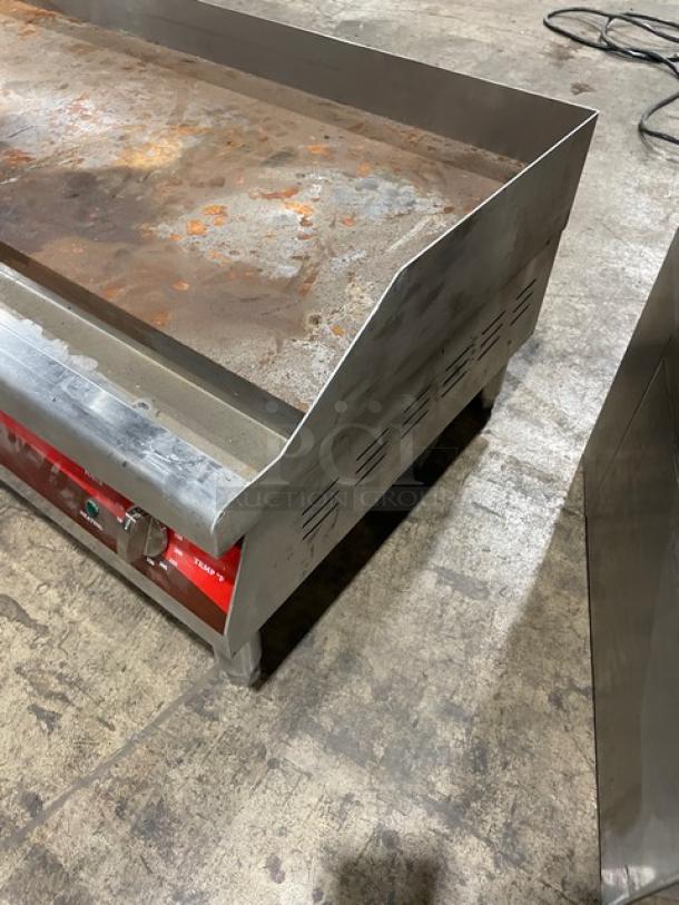 Commercial flat-top griddle with rust spots and stainless steel sides, showing signs of wear. Red control panel with knobs.