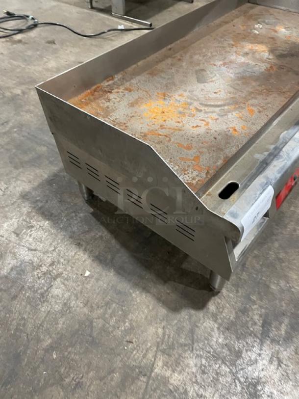 Stainless steel commercial griddle with rust and wear, vented sides, mounted on four legs. Used condition, tags partially visible.