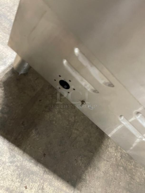 Stainless steel commercial kitchen appliance, lower section. Shows a vent hole and some light scuffing.