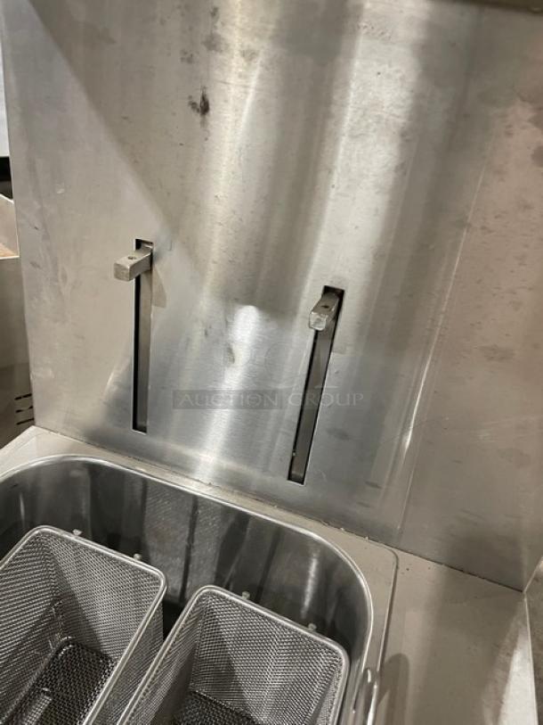 Commercial stainless steel deep fryer with dual fry baskets, visibly used condition, some surface marks, ideal for restaurant use.