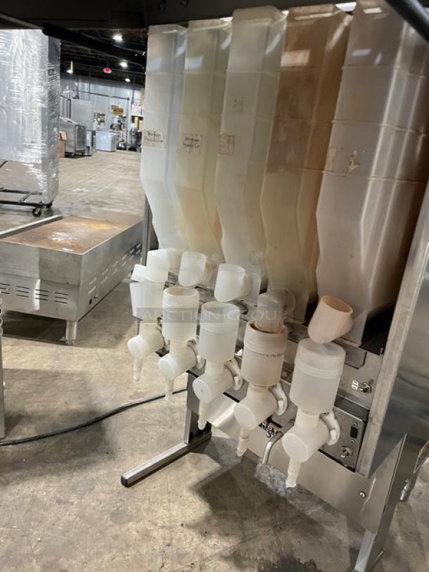 Commercial beverage dispenser with multiple containers and spouts, stainless steel frame, used condition, minor wear visible.