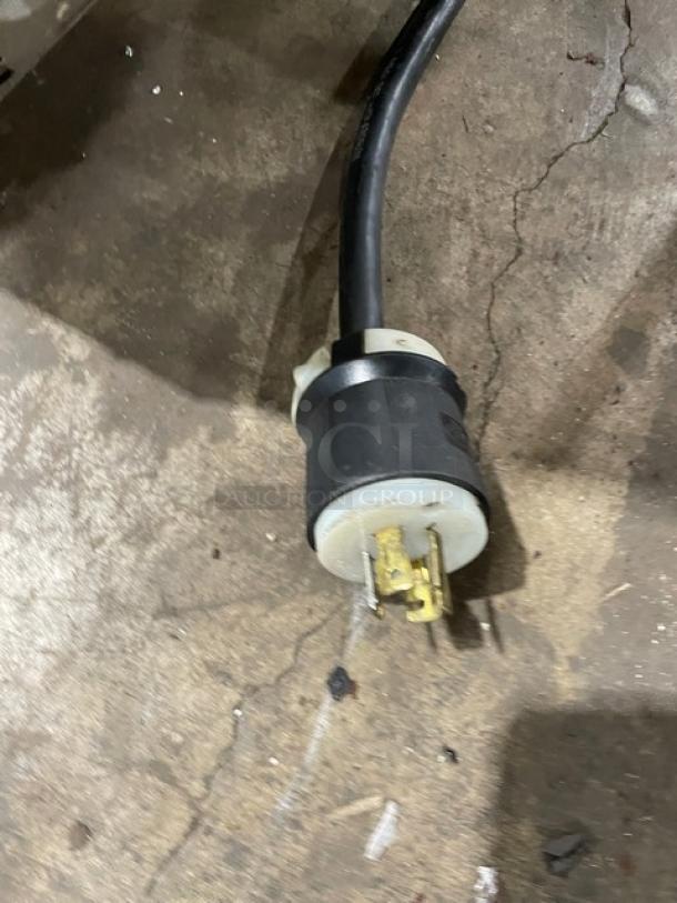 Heavy-duty electrical plug with black casing and brass prongs, in good condition, on concrete floor.