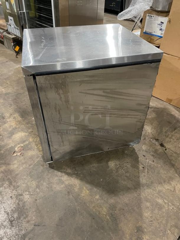 Stainless steel square refrigeration unit, scuffed surface, on a concrete floor, no visible labels or markings.