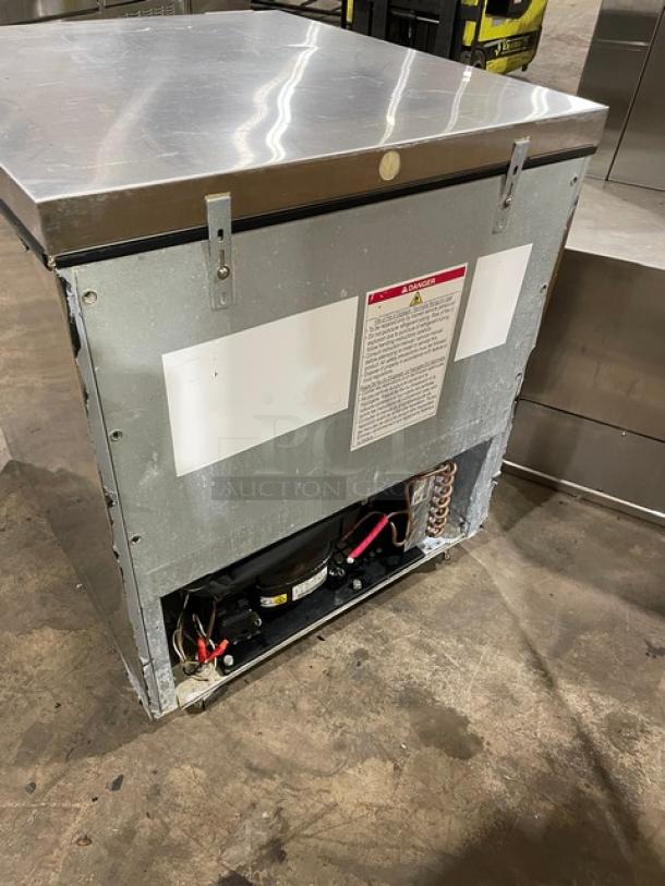 Industrial stainless steel ice machine with visible compressor, in used condition. Safety instructions label displayed.