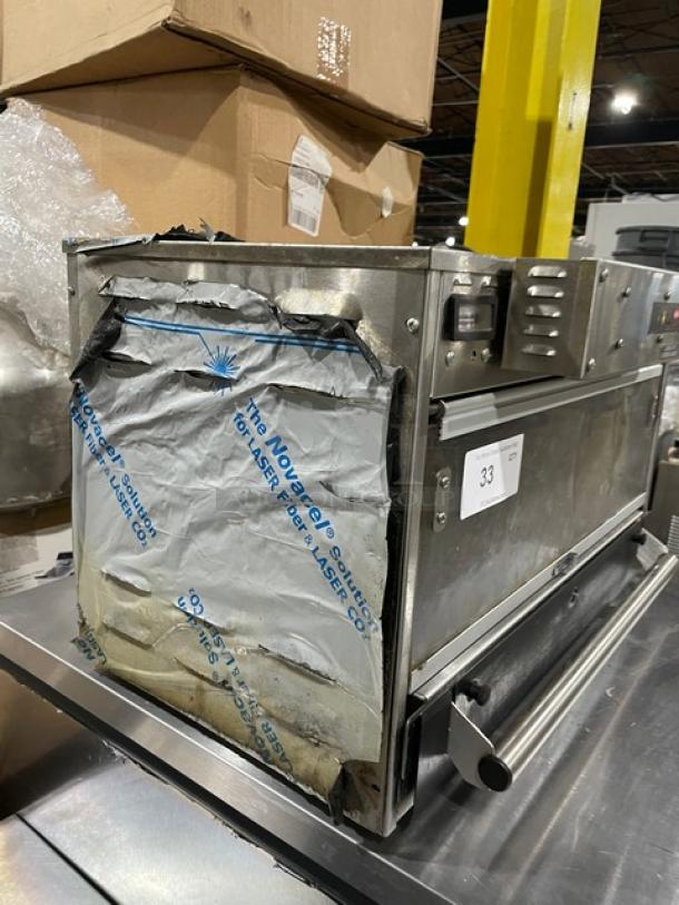 Commercial stainless steel appliance, protective covering partially removed, labeled "The NovaTech Laser." Auction tag with number 33 attached.