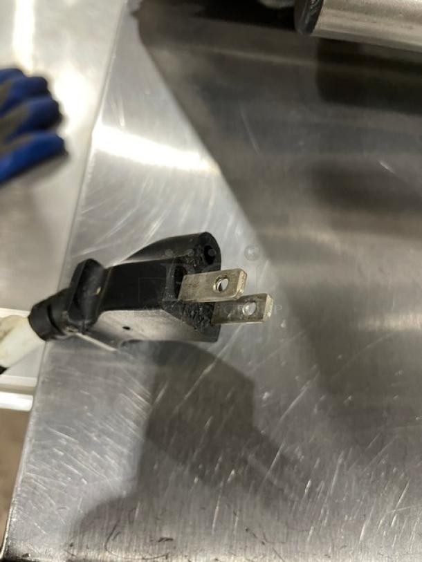 Black two-prong power plug with attached cord on metal surface, in good condition.