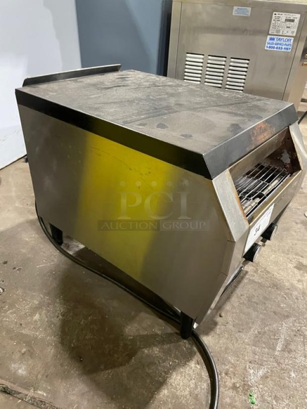 Commercial bread toaster in used condition with stainless steel exterior. Features adjustable conveyor, steel grate. Identifying label visible.