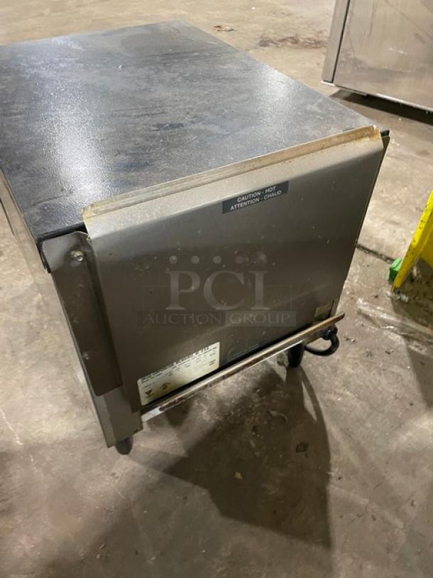 Industrial stainless steel warming cabinet with visible surface wear. Label reads "Caution: Hot." Features sturdy legs.