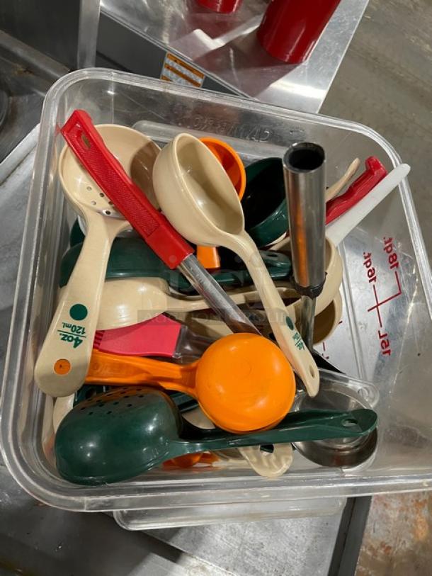 Box of assorted kitchen utensils including spoons and ladles in various colors, some marked with measurements.