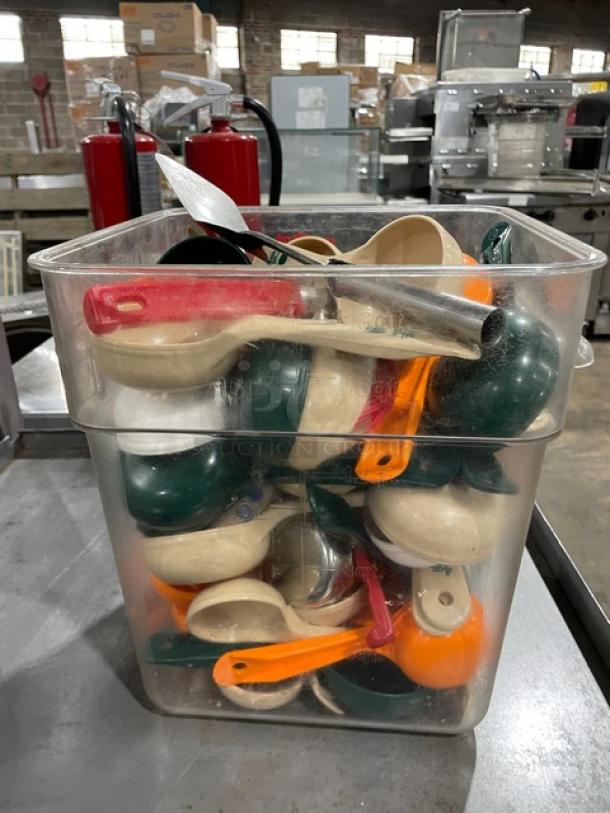 Clear plastic bin filled with assorted kitchen scoops in green, orange, and beige with red handles; used condition.