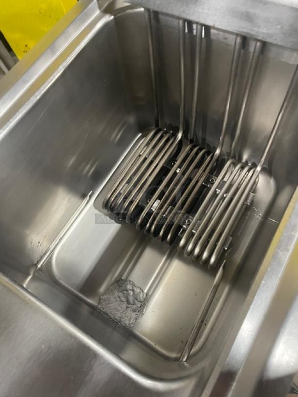 Commercial deep fryer tank with heating elements, stainless steel, used condition, visible oil residue at the bottom.