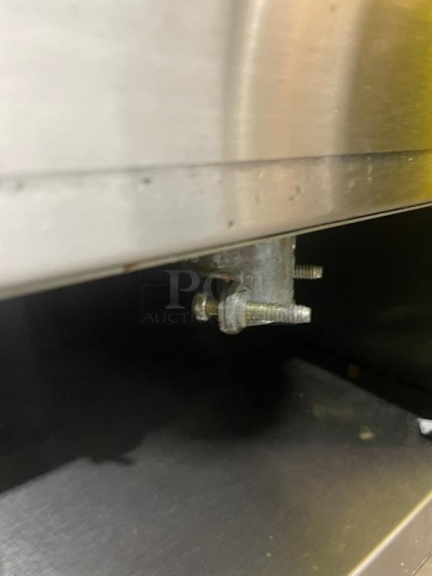 Metallic adjustable screw and bracket mechanism under a stainless-steel appliance, showing wear, designed for leveling or securing.